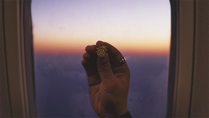 a fireball pin held by a hand up against an airplane window with a horizon in the background