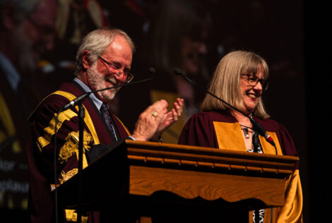 Patrick Deane claps as Donna Strickland laughs at the podium at convocation