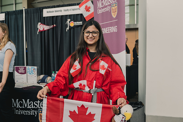 A student in a red jumpsuit with Canadian flags adorning it holds up another Canadian flag.