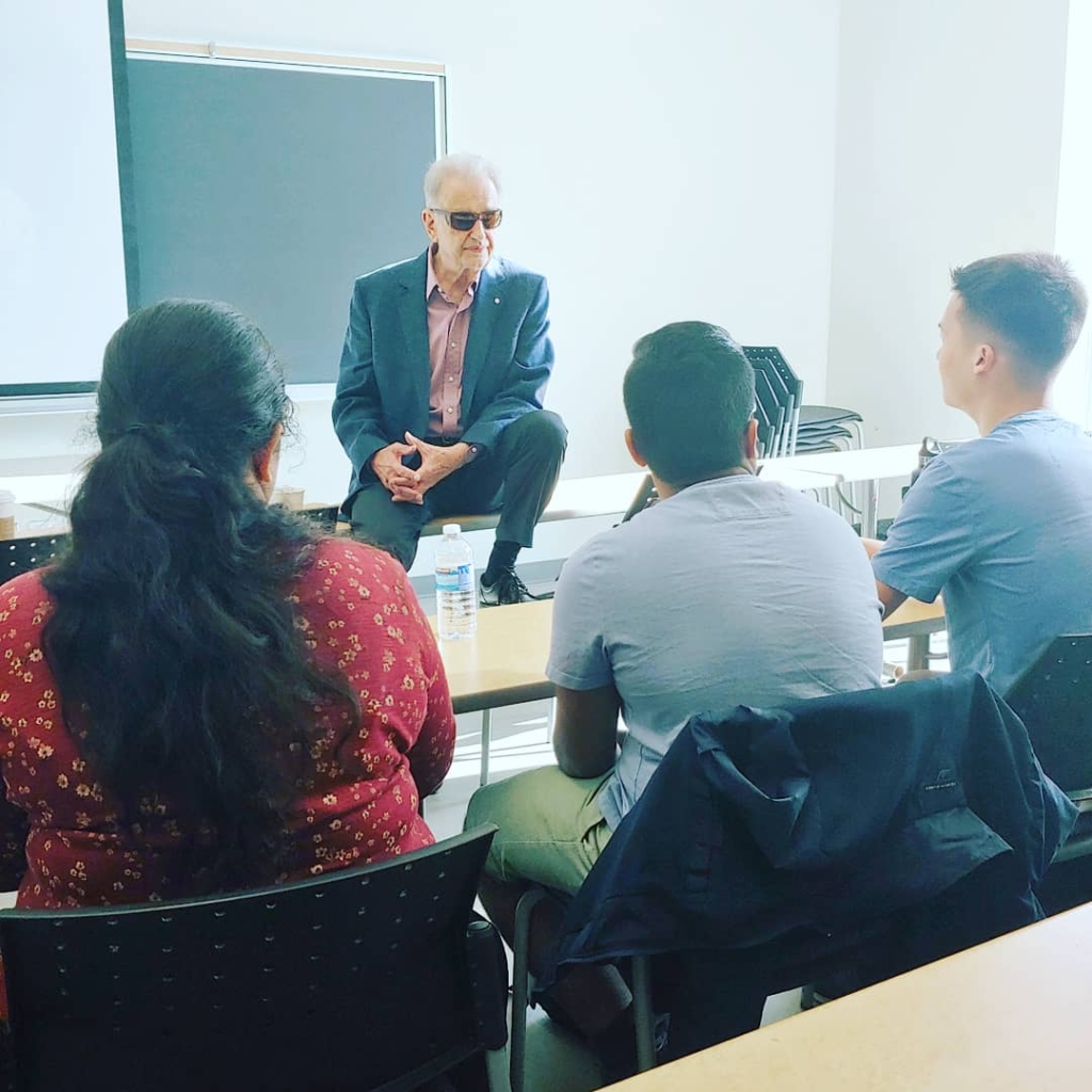 John Bandler sits on a table while talking to students