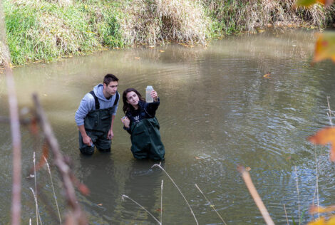 two students stand in water inspecting a bottle filled with water from the river