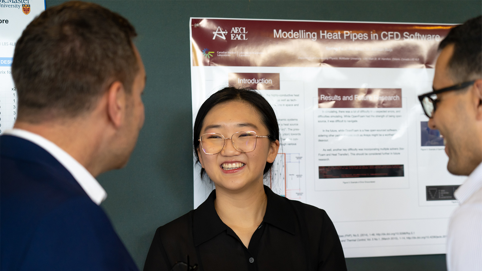an undergraduate researcher smiles as they share their research with two attendees