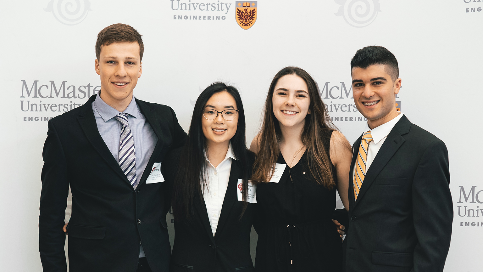 four students stand with their arms around each other in front of a Mac Eng logo backdrop