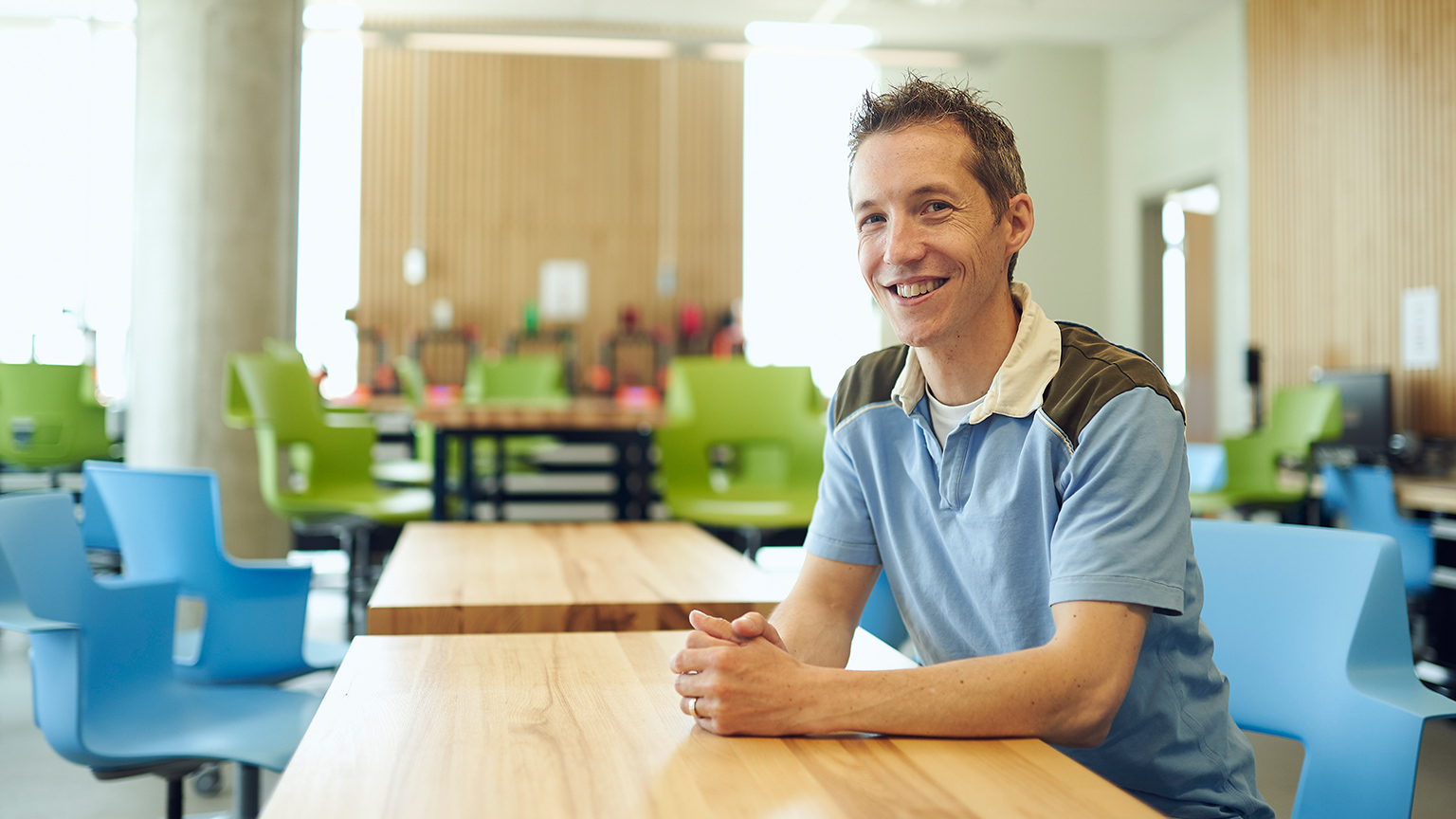 Colin McDonald sitting in an empty classroom with colourful green and blue chairs