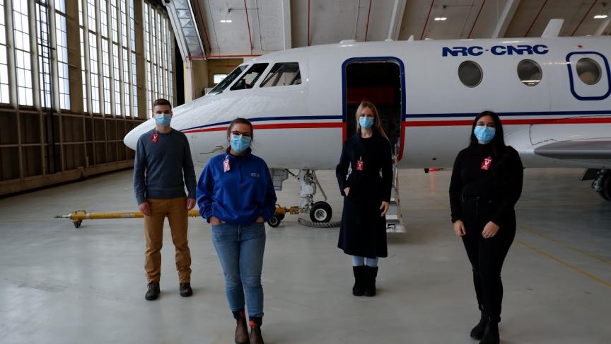 four people stand in front of a plane