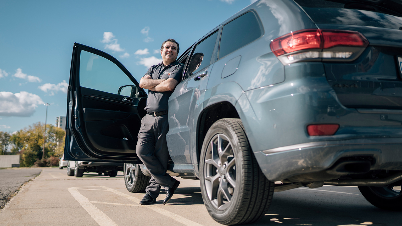 Ali leans up against the drivers side of a car with the door open