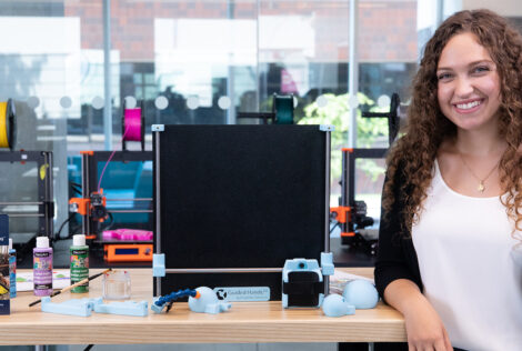 Lianna stands beside her guided hands device in the iBioMed Design Studio