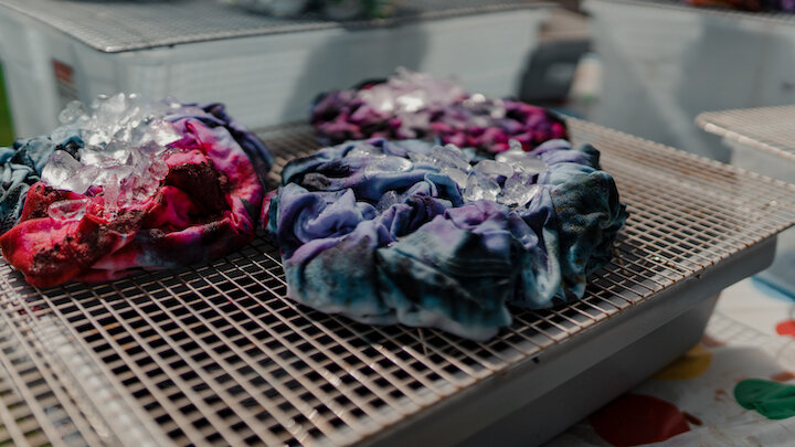 scrunched up tie dye T-shirts sitting on a rack that have ice on top of them. 