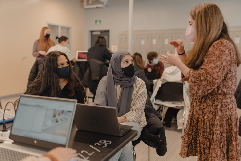 A teaching assistance explains something to two students