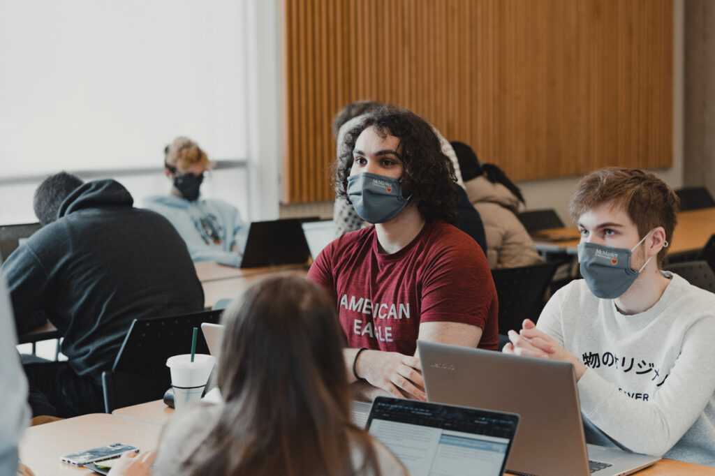 two students sitting at a desk with laptops wearing McMaster face masks