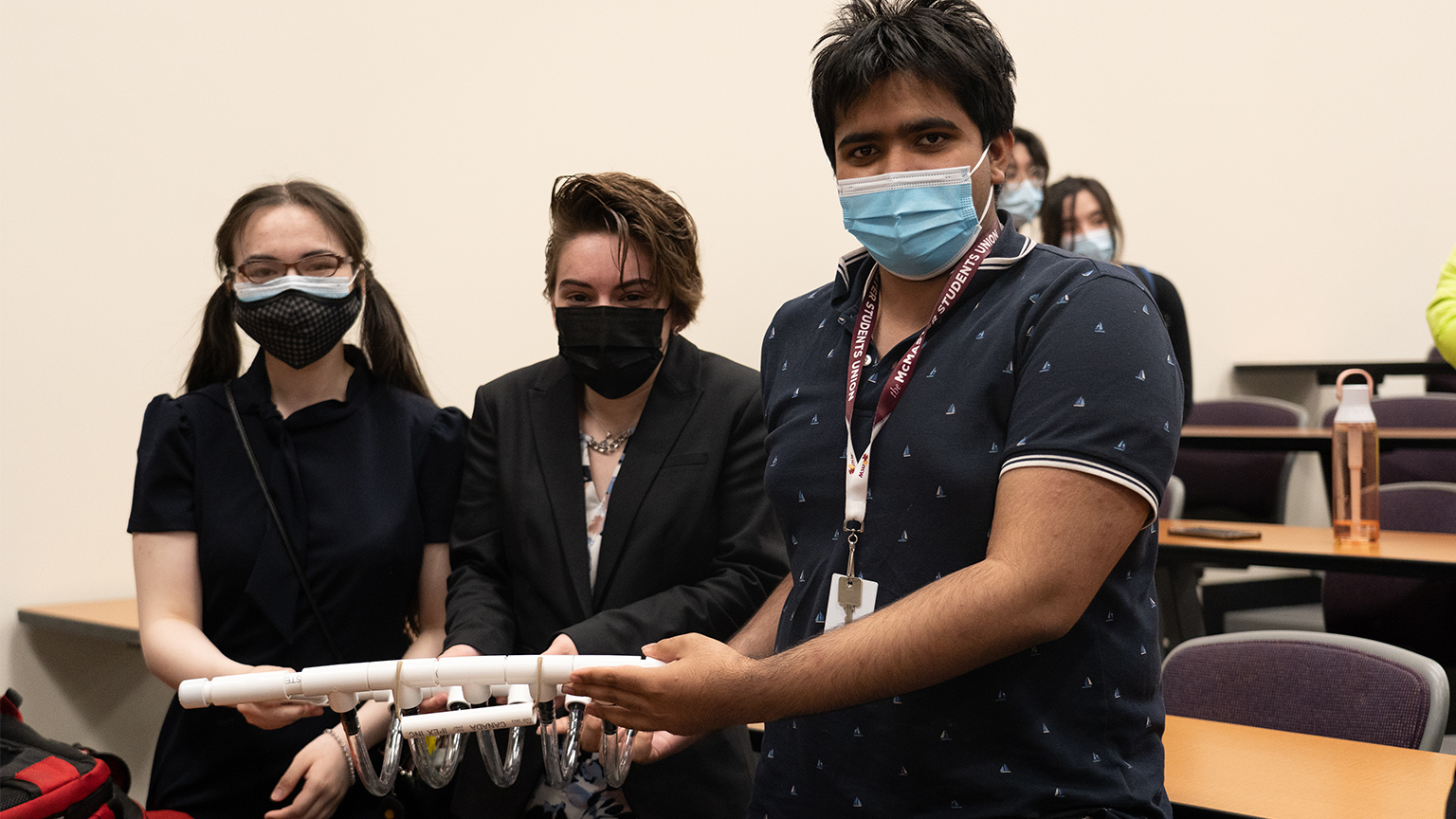 Three students stand holding their invention that assists in washing dishes.