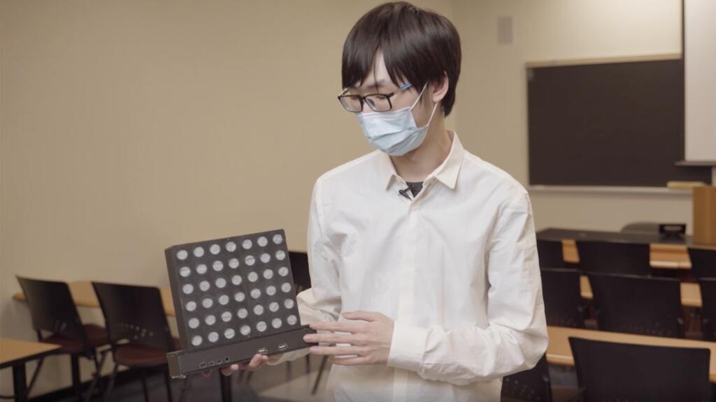 A student holds an LED board game. The lights are in a grid.