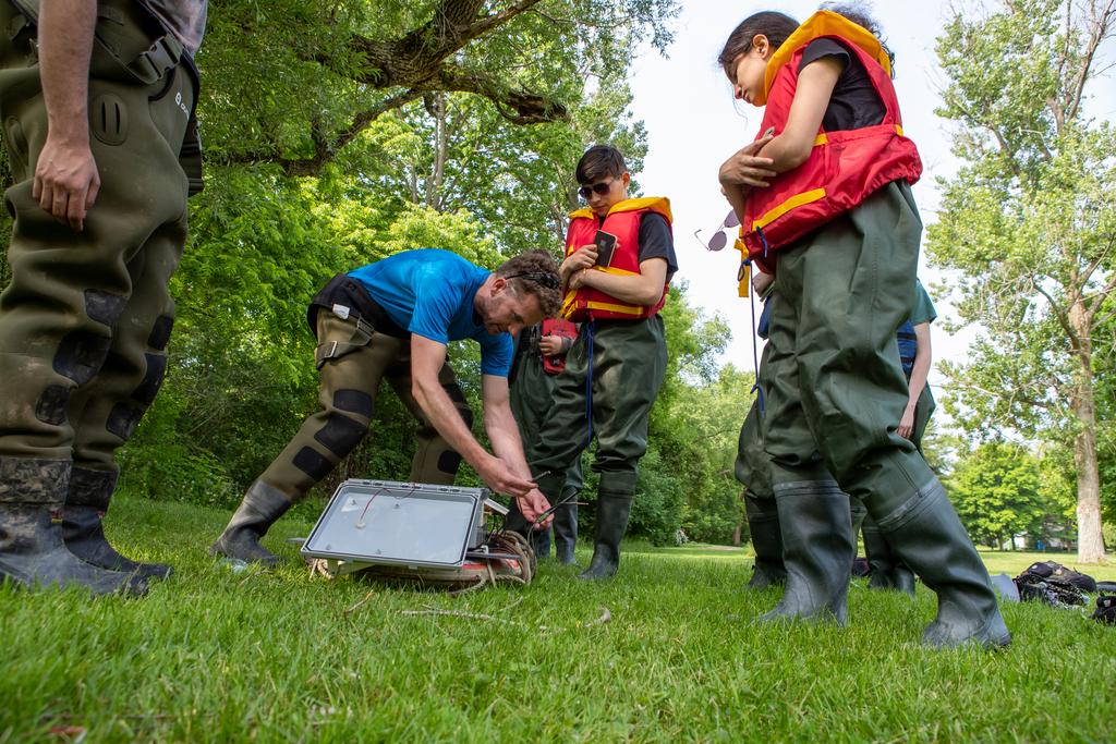 Charles de Lannoy bends over equipment with students standing around him.