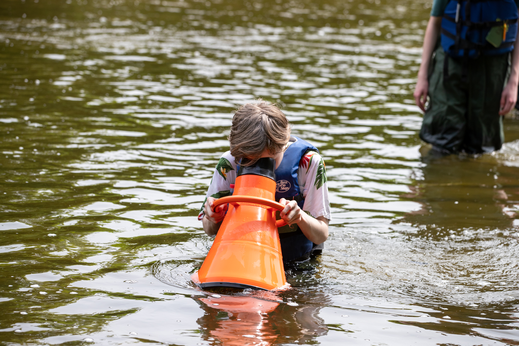 A student looks through an orange cone into the water.