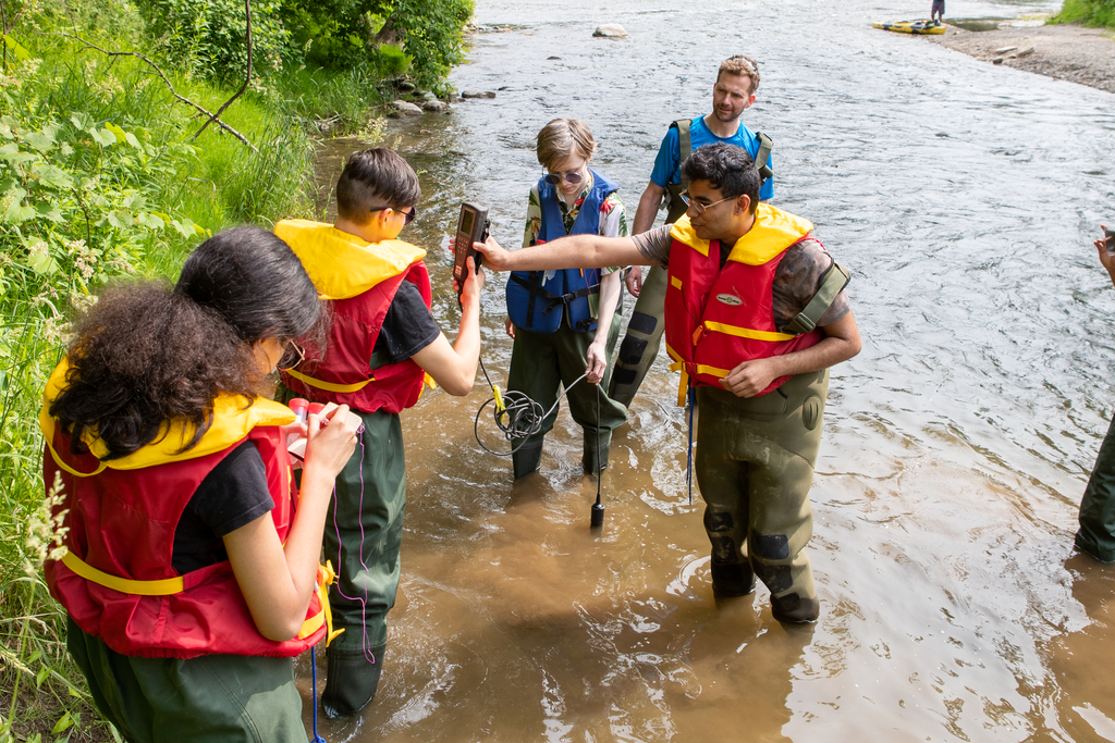 Students gathered in the river inspect something they've found