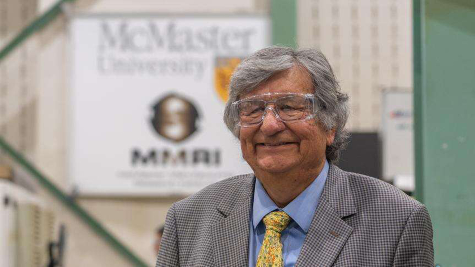 Barry Hill smiles while wearing safety glasses in front of a McMaster MMRI banner.
