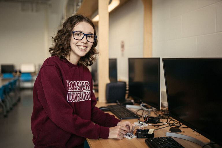 Julia Dowson, wearing a McMaster sweater, tinkers with robotics on a table with computers.