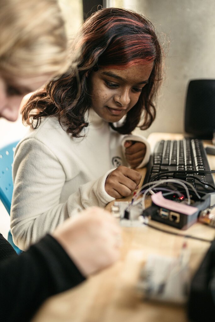 Neaha Bijo looks closely at some robotics on a table. Another student is pictured in the foreground.