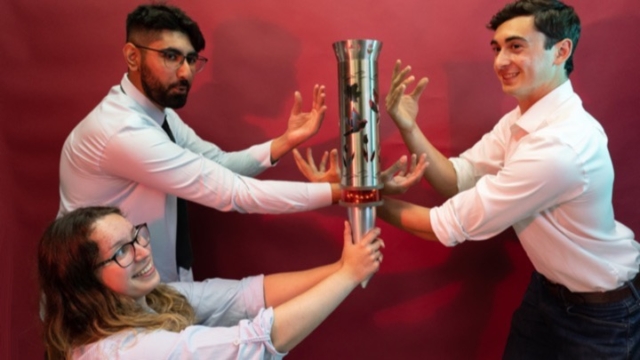 three people posing with an unlit torch using their hands to imitate the flames
