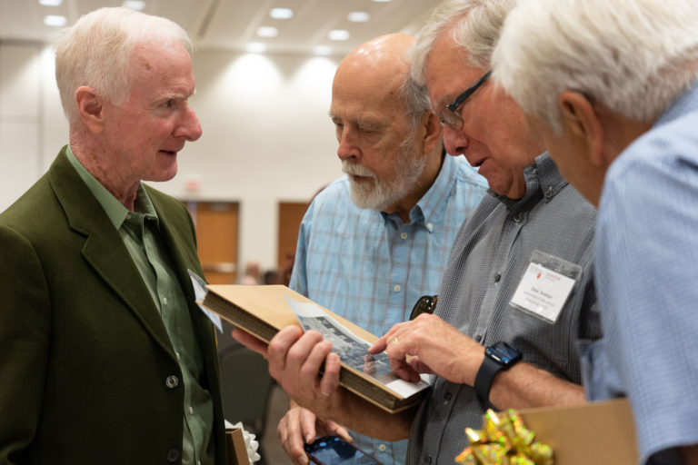 four men huddled together with a photo in their hands