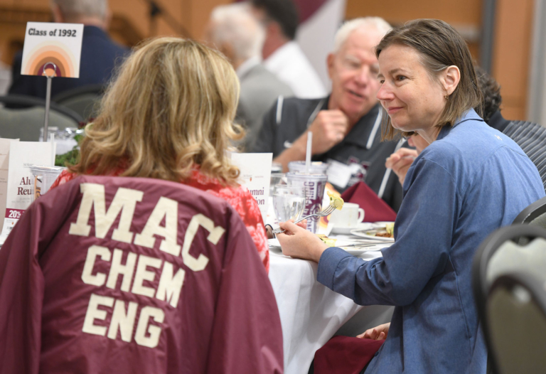 two women speaking to each other, a Mac Chem Eng jacket hangs off one of the chairs they are sitting in