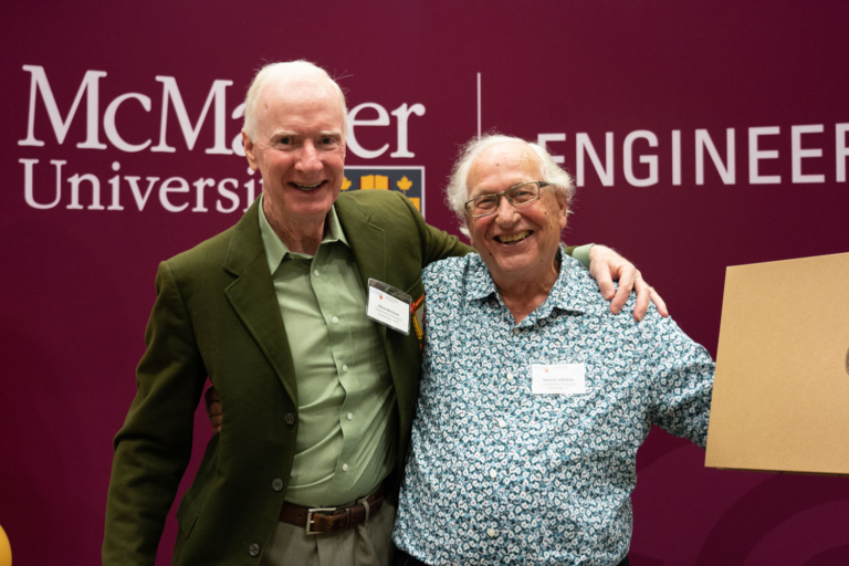 Two grads pose together with their arms extended in celebration