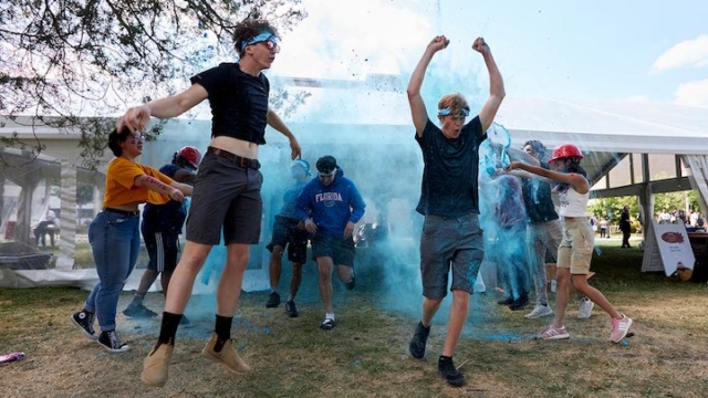 group of people running in blue powder with their hands raised.