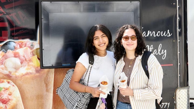 two girls holding pizza cones from a food truck.