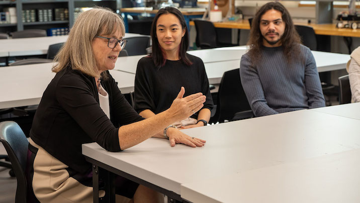 Donna Strickland speaking to students in a classroom, two students sit beside her looking in admiration