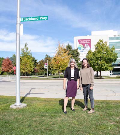 Donna Strickland standing beside new street sign that has her last name on it.