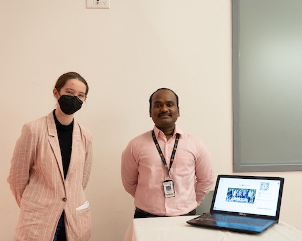 two people standing behind a laptop.