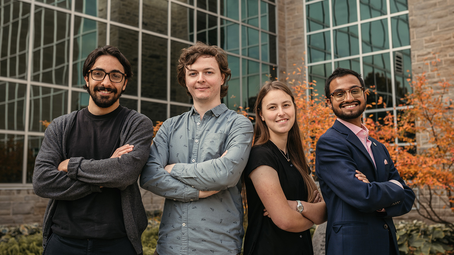 four people standing in front of a building with their arms crossed in front of them.