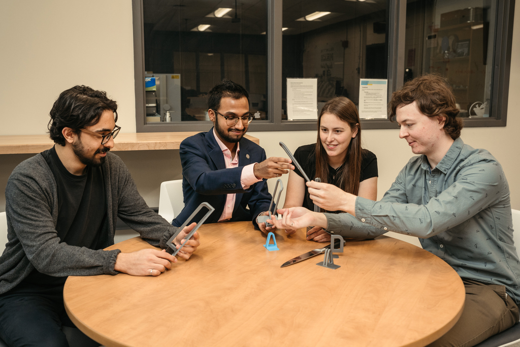 four people sitting at a round table examining a plastic object.