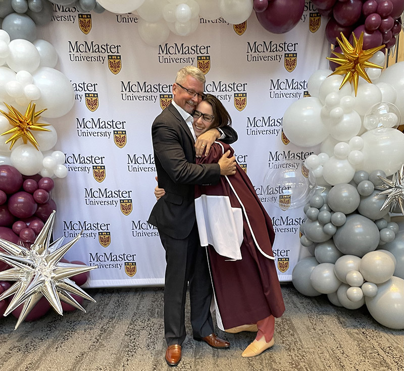 Grad and alumni father hugging at Convocation in front of a backdrop with balloons