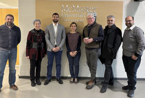 A group of people stand in front of a McMaster University sign.