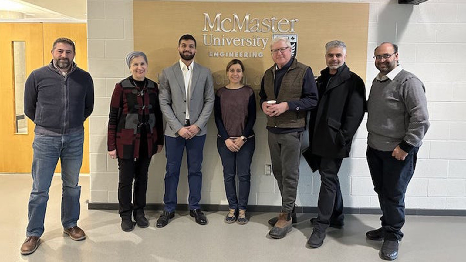 A group of people stand in front of a McMaster University sign.