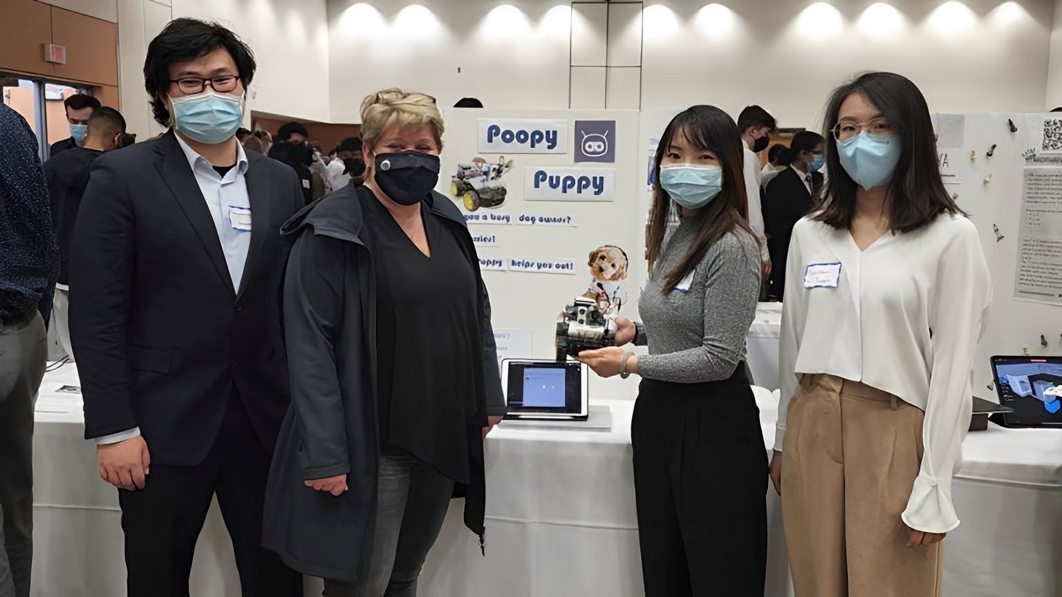Heather Sheardown poses with the Poopy Puppy Capstone group. One member holds a robot that can find your pets excrement.