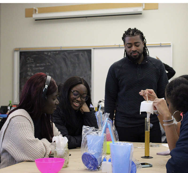 Student participants in Black Outreach STEM series around a table with an experiment in progress
