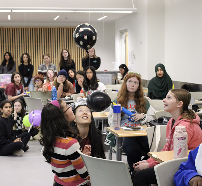 Girls at a STEM activity session on McMaster's campus, working on an experiment with a balloon