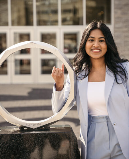 Student smiling in a blue suit by the iron ring statue