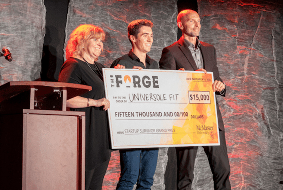 man holding between two people on stage holding a large check.