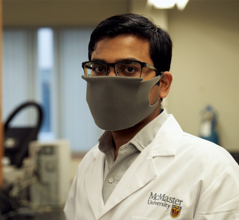 A person wearing a mask and a McMaster University lab coat.
