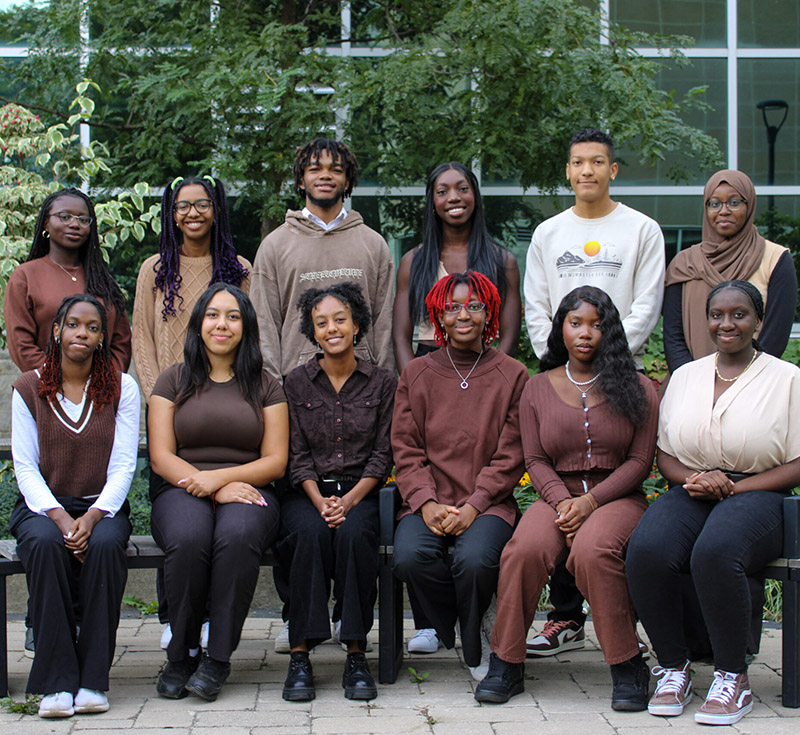 Members of NSBE's McMaster chapter sitting in two rows outside of JHE on McMaster's campus