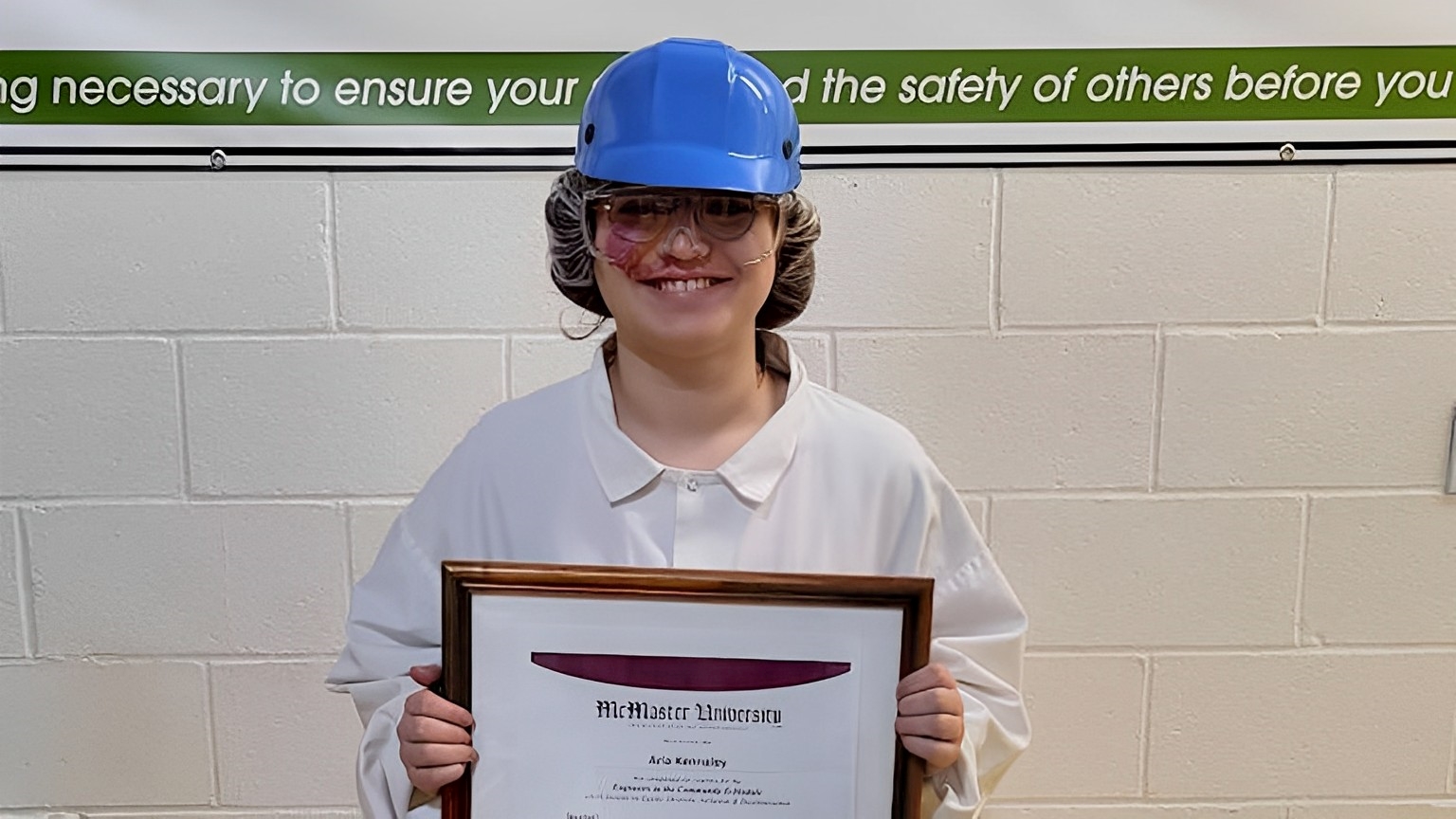 person at work wearing a hard hat and holding up a framed certificate.