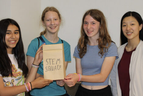 Four girls holding up a paper bag with the words STEM Squad written on it
