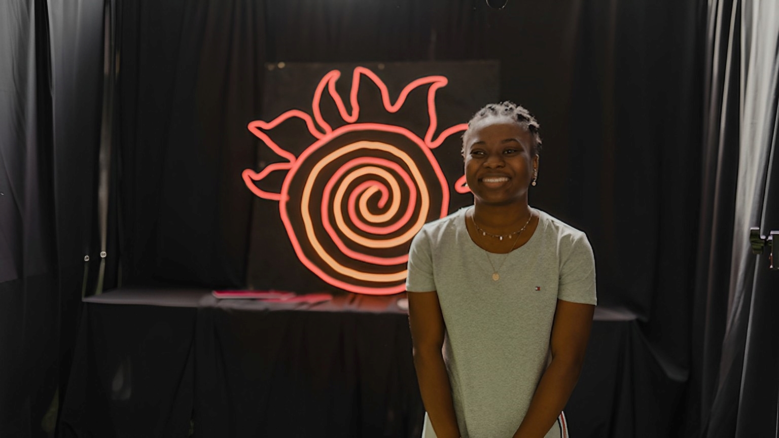 person standing in front of a neon sign shaped like a fireball.