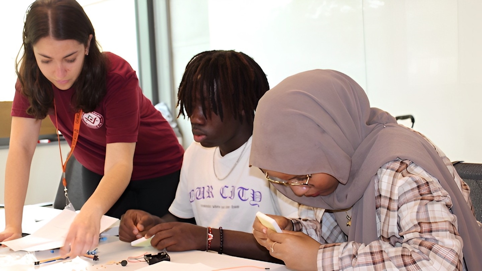 A Venture staff members supports two Black students on a STEM activity