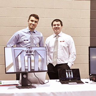 Two students at the capstone showcase standing behind a computer screen and display