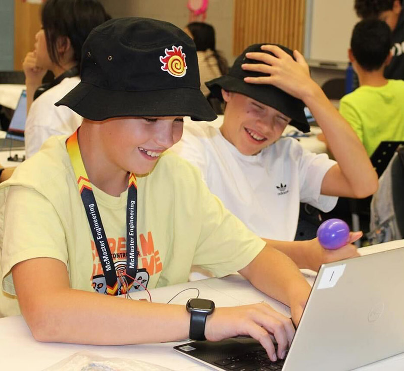Smiling young students at a McMaster Engineering outreach event, working at a laptop