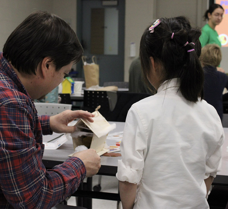 Child and parent working on a STEM activity with their backs turned to the camera